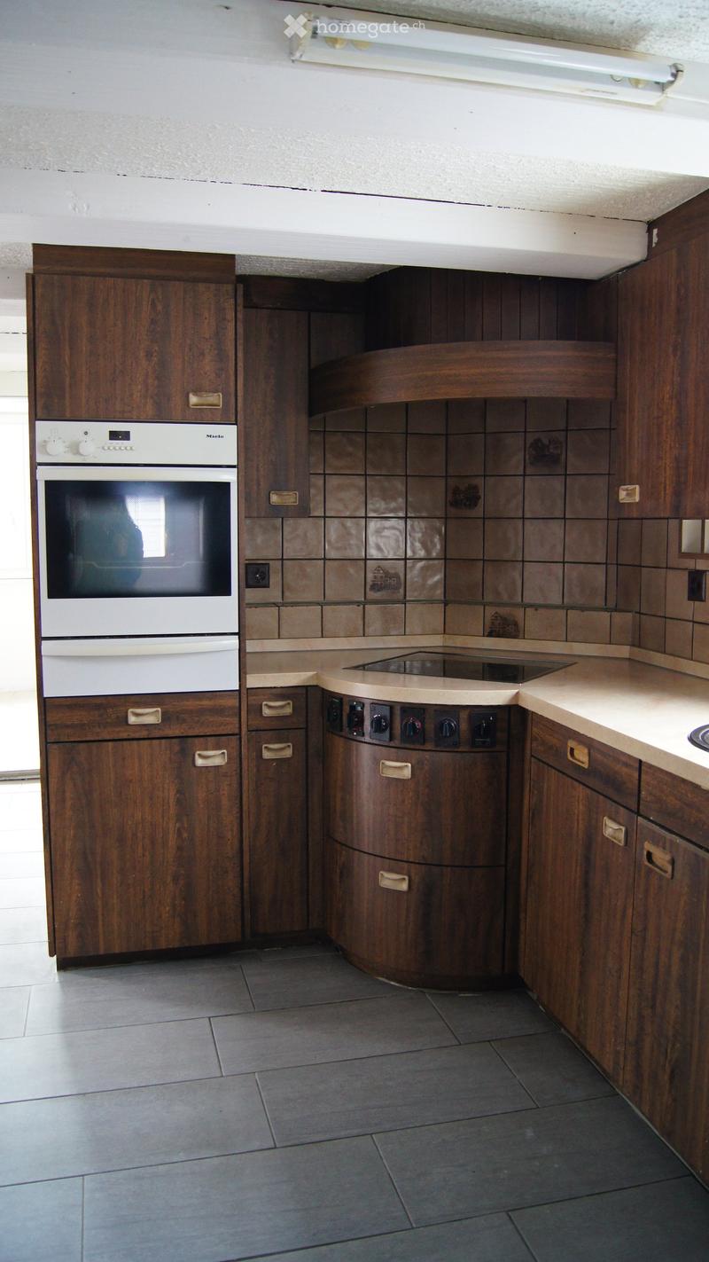Kitchen with wooden cabinets, a white oven, and an induction cooktop, featuring tiled backsplash and tiled flooring.