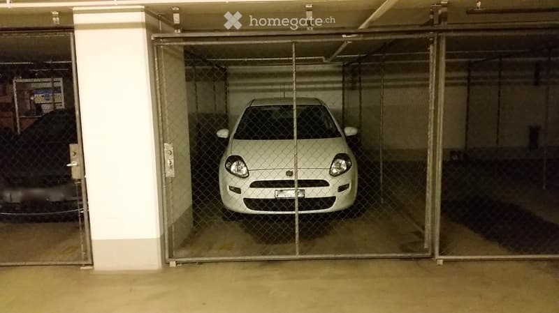 Underground parking area with a single white car parked inside, secured by a metal gate.