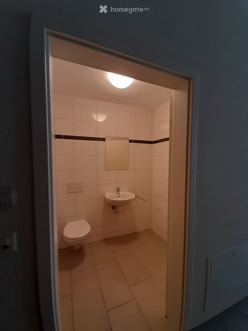 Small bathroom with white tiled walls and floor, featuring a toilet, sink, and mirror.