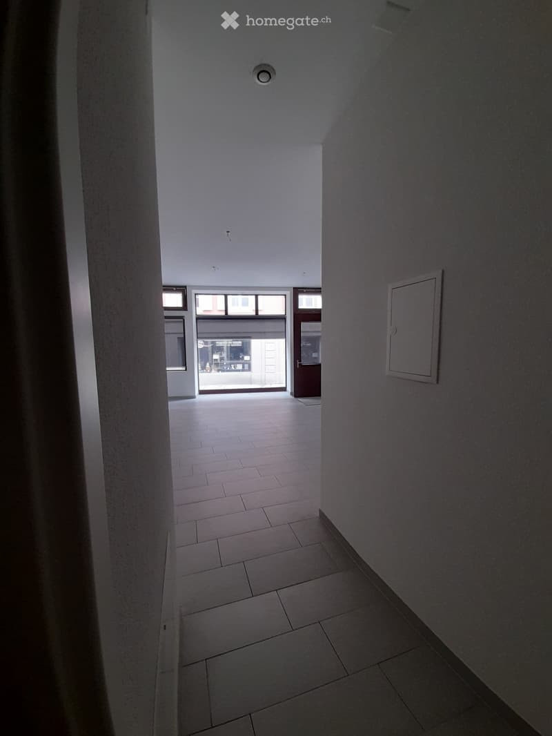 Empty hallway with tiled floor, white walls, and a door leading to an exterior area.