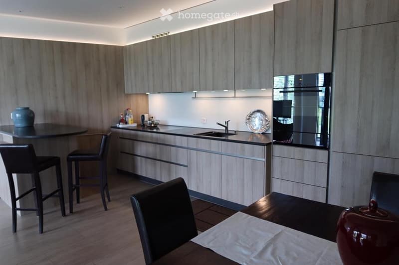 Modern kitchen with light wood cabinets, stainless steel appliances, bar stools, dining table, and decorative items.