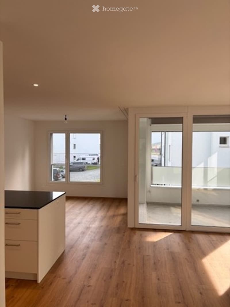Empty room with wooden flooring, large windows, and sliding glass doors leading to a balcony area.