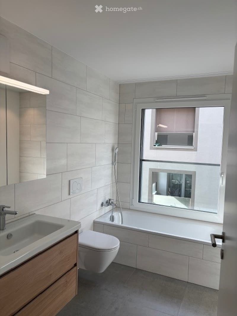 Modern bathroom with white tiles, a large window, a sink with a modern faucet, a toilet, and a bathtub.