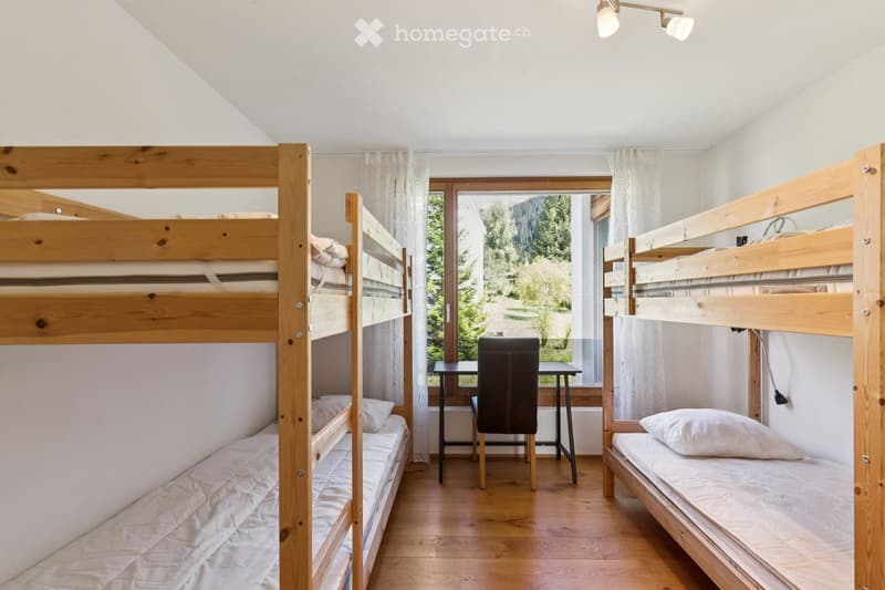 Cozy room with wooden bunk beds, a small table, and a chair, overlooking a scenic outdoor view.