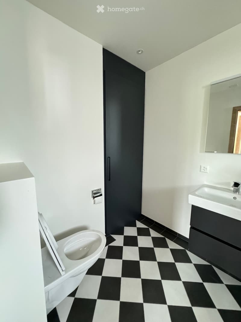 Modern bathroom with white walls, black and white checkered floor, toilet, sink, and mirror.