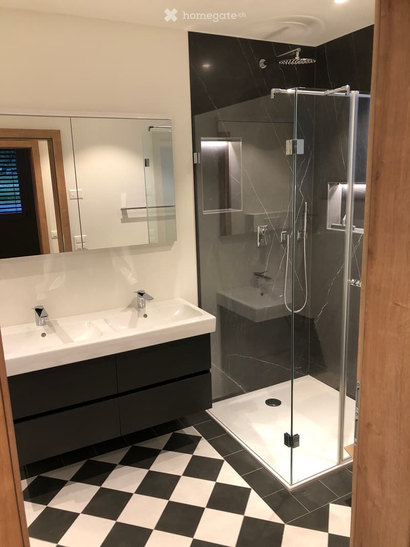 Modern bathroom with black and white checkered floor, white sink with chrome faucet, large mirror, and glass-enclosed shower with modern fixtures.
