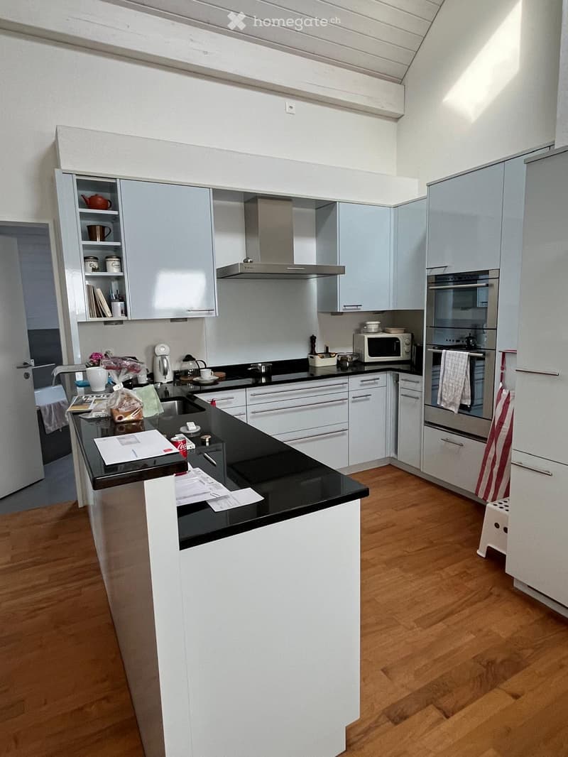 Modern kitchen with white cabinets, black countertops, and wooden flooring. Includes a refrigerator, oven, microwave, sink, and various kitchen appliances.