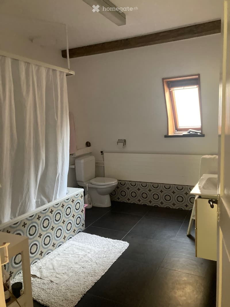Bathroom with a toilet, bathtub, sink, shower curtain, and a white rug on the floor.