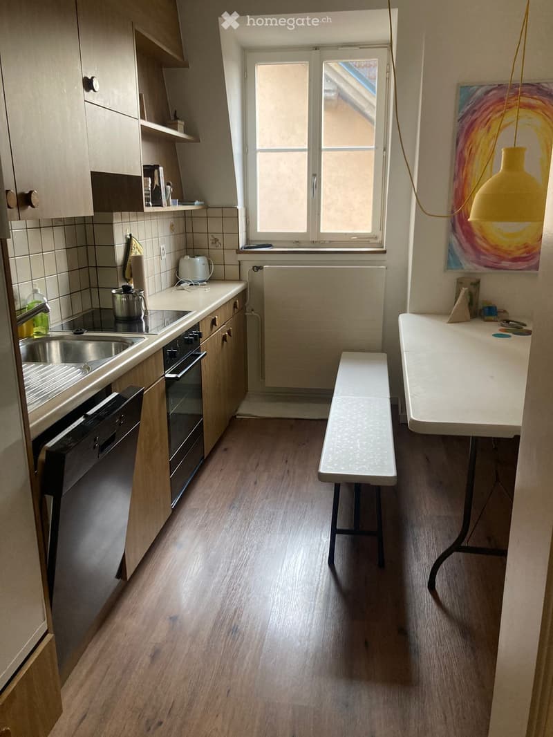 Modern kitchen with wooden flooring, white cabinets, stainless steel appliances, a bench, and a table.