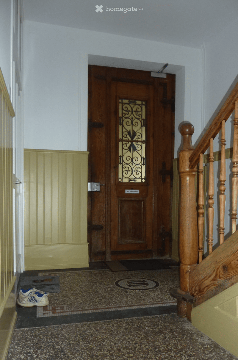 Hallway with wooden staircase, double doors with glass panels, patterned tile floor, and a small rug near the entrance.
