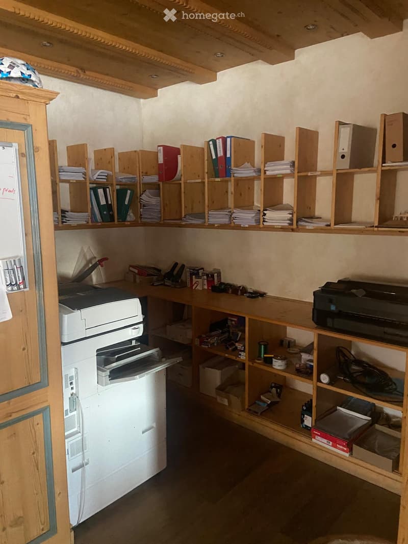 A small, organized room with wooden shelves filled with folders and binders, a desk with a printer, and various office supplies.