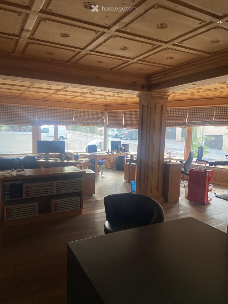 Office space with wooden floors, large windows with checkered blinds, multiple desks, chairs, computers, and cabinets.