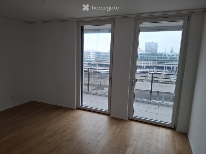 Empty room with wooden flooring and large sliding glass doors leading to a balcony with a city view.