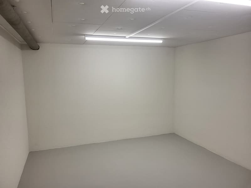 Empty room with white walls, grey carpeted floor, and a white drop ceiling with recessed lighting.