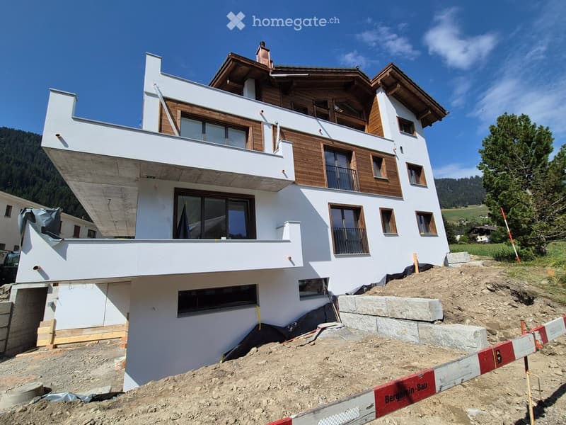 Modern, multi-story house with white walls, wooden accents, and large windows, under construction with exposed scaffolding and construction materials.