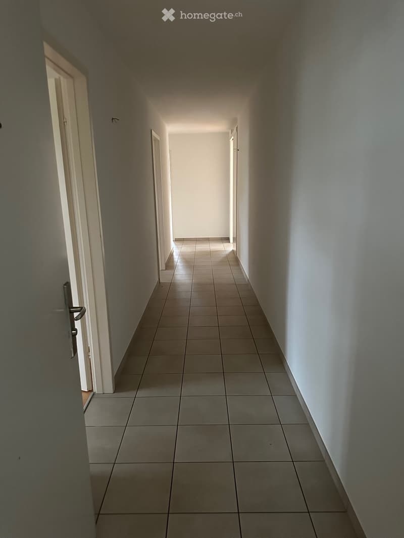 Empty hallway with tiled floor and white walls, featuring several doors on both sides.