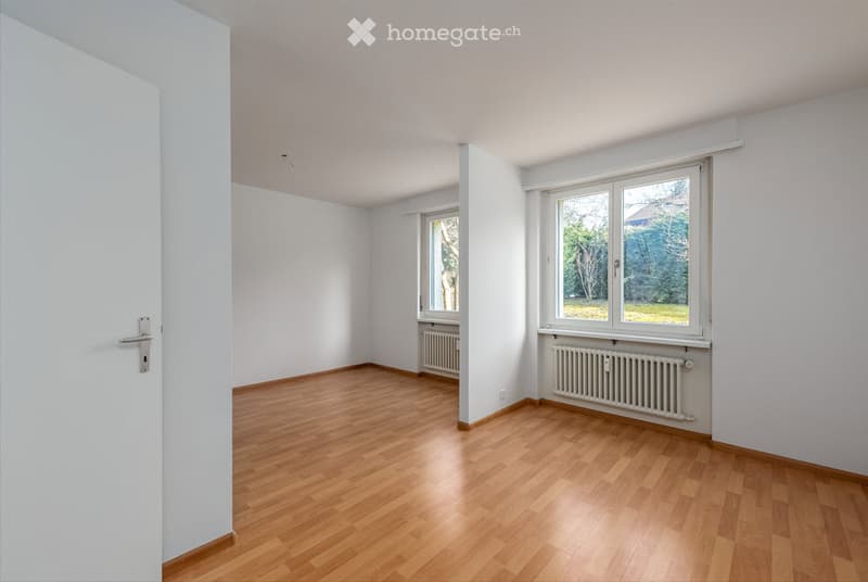 Empty room with wooden flooring, white walls, and two windows with radiators beneath them.