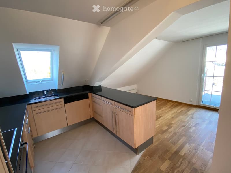 Modern kitchen with light wooden cabinets, black countertop, sink, and a window. The floor is wooden, and there is a sliding glass door leading outside.
