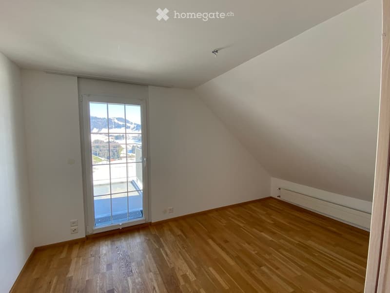 Empty room with wooden flooring, white walls, and a large window with a view of the outdoors.