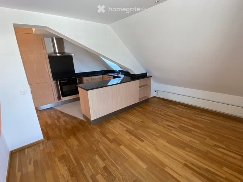 Modern kitchen with wooden flooring, light-colored cabinets, black countertop, and stainless steel appliances including an oven and range hood.