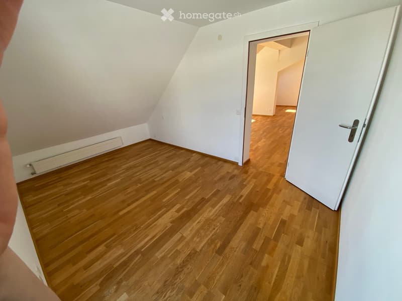 Empty room with wooden flooring and white walls, featuring a partially open door leading to another room.