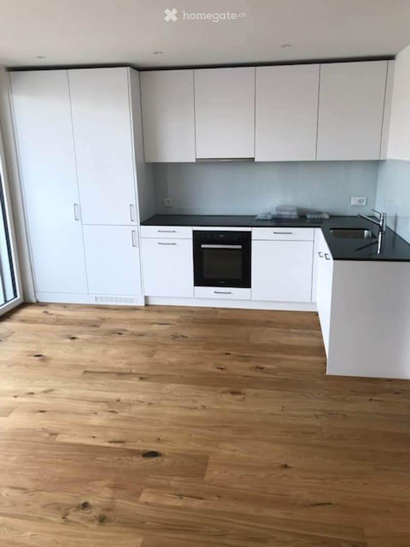 Modern kitchen with white cabinets, black countertops, and a wooden floor. Features an oven and a sink.