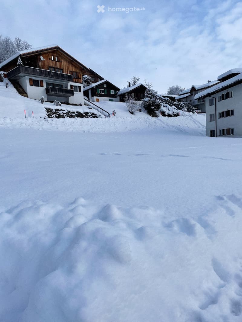 A cluster of houses in a snowy landscape, featuring wooden and white facades, balconies, and snow-covered roofs.