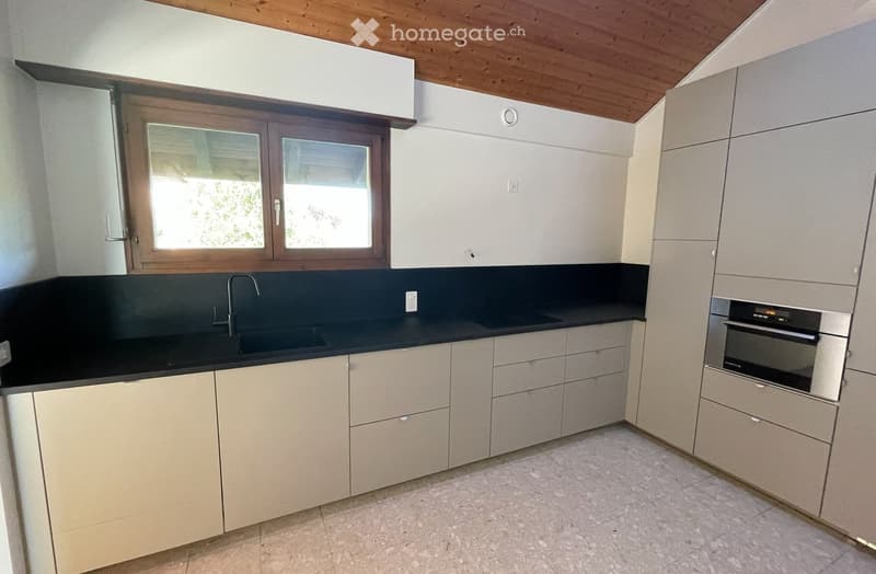 Modern kitchen with light-colored cabinets, black countertops, a sink with a faucet, and an oven. The room features a wooden ceiling and a window with wooden frames.