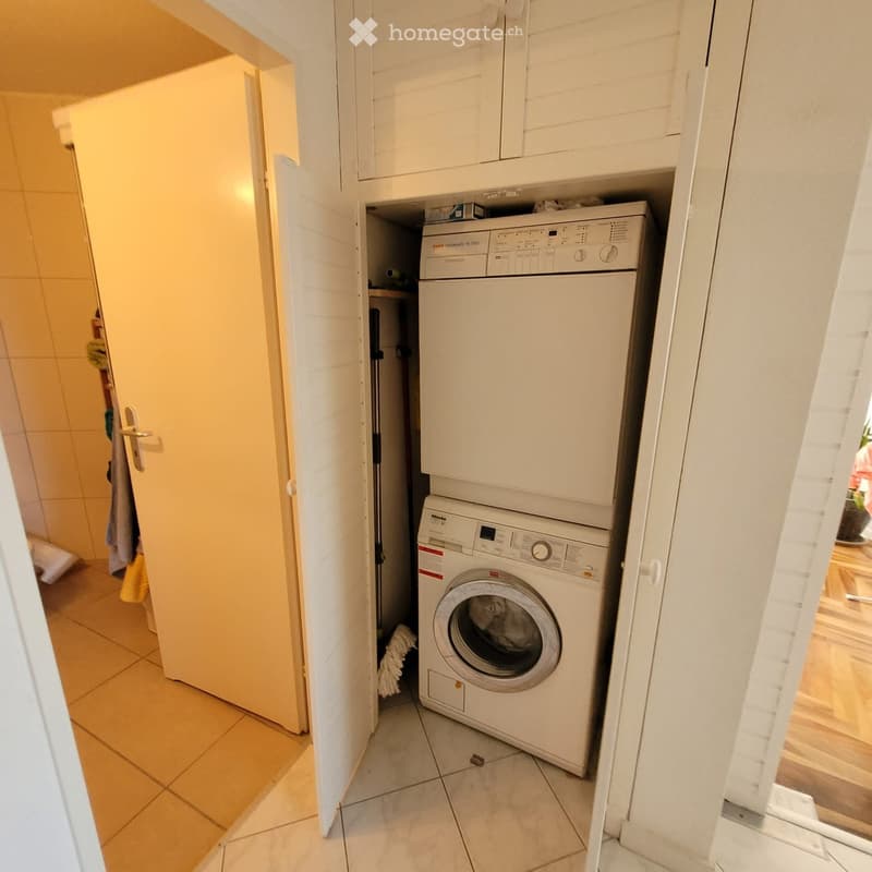 Compact bathroom with a white washing machine and a white dishwasher stacked vertically, tiled floor, and white cabinetry.