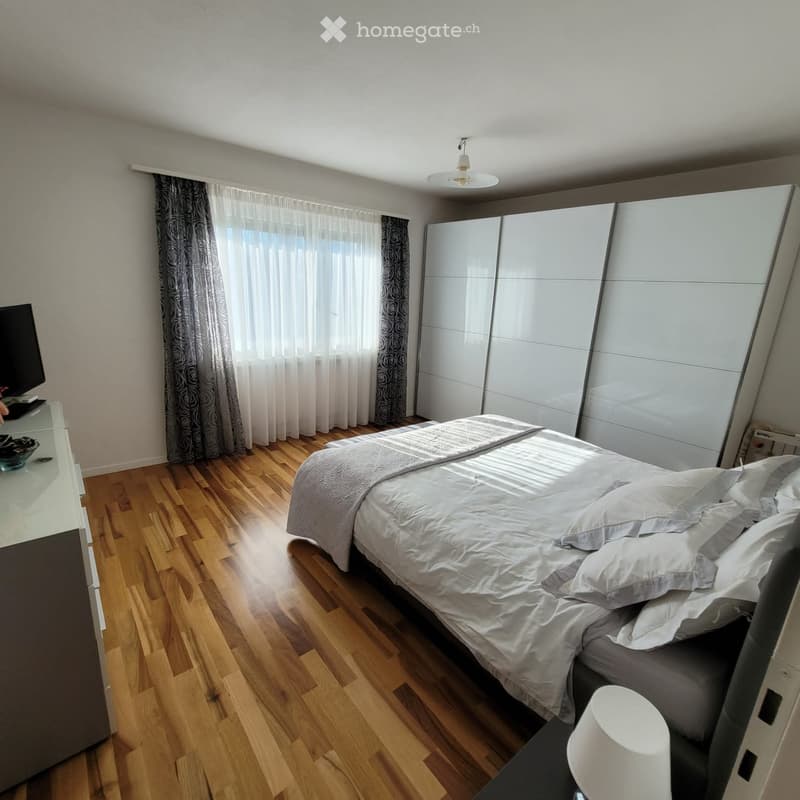 Modern bedroom with wooden flooring, large bed with white bedding, wardrobe, and large window with curtains.