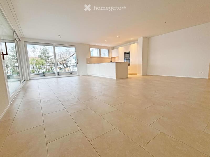 Empty room with large sliding glass doors leading to a balcony, white tiled floor, and a small kitchen area with white cabinets and a countertop.