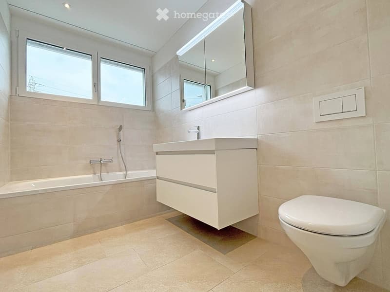 Modern bathroom with beige tiles, a bathtub, a sink with a mirror, and a toilet.