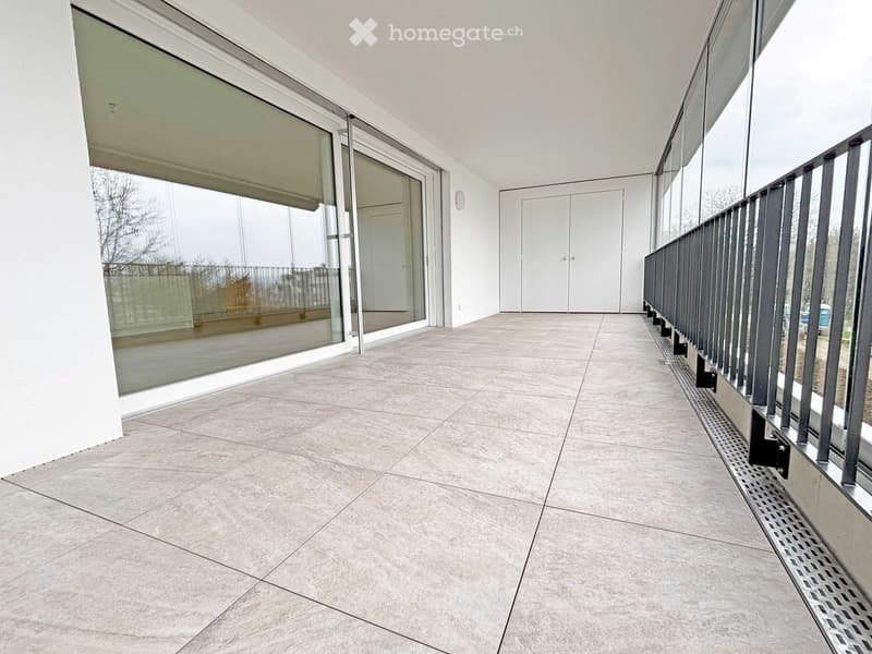 Modern balcony with large glass sliding doors, tiled floor, metal railing, and a view of the surrounding area.