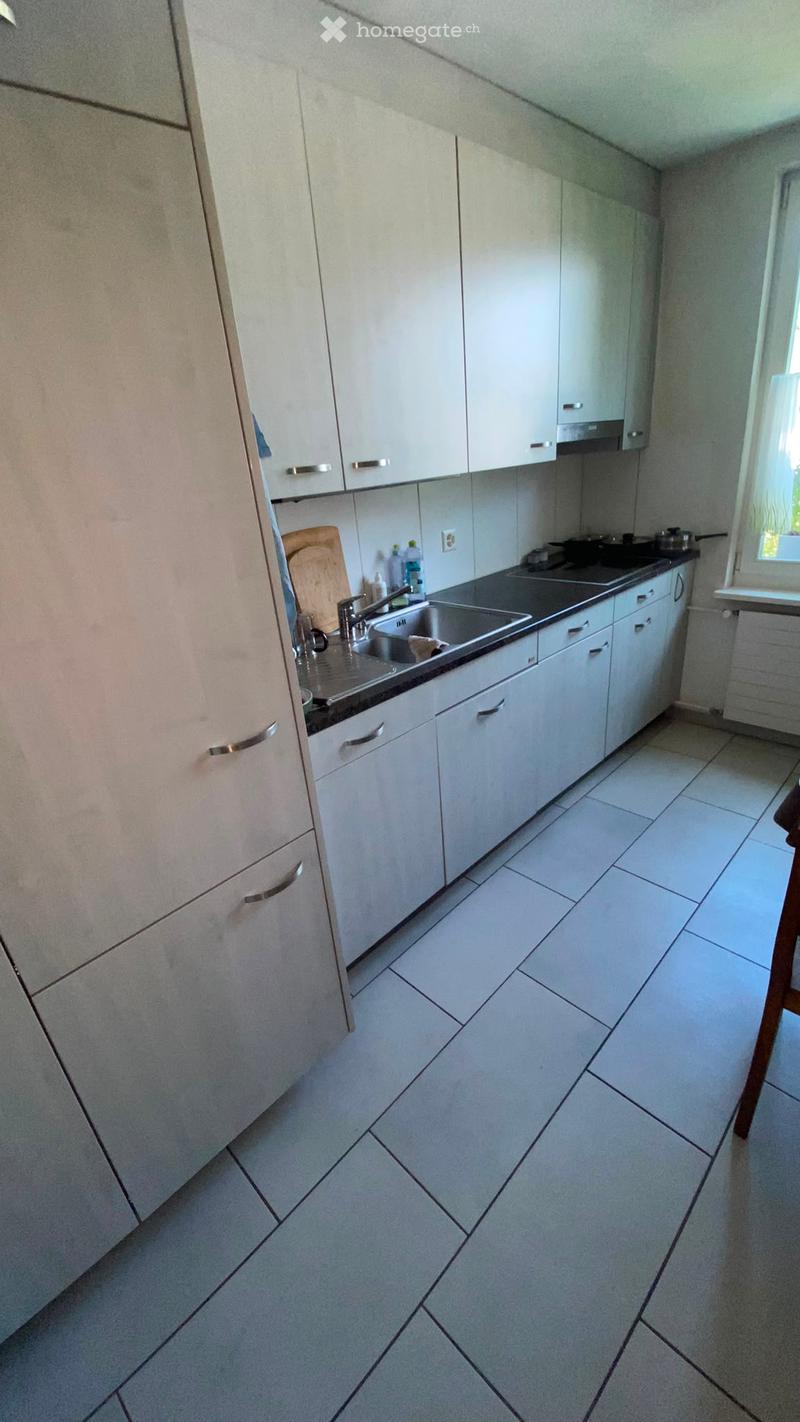 Modern kitchen with white cabinets, tiled floor, and stainless steel sink.