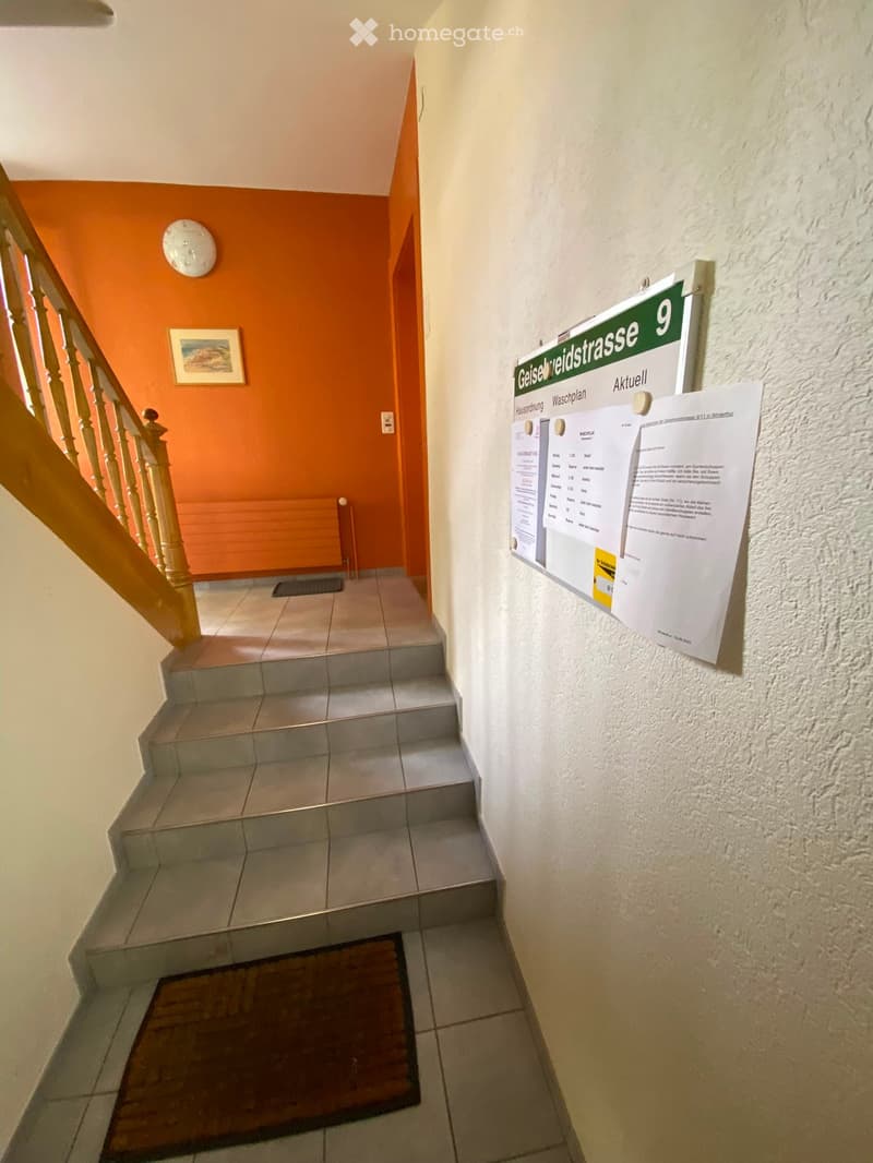 Staircase with wooden railing, tiled steps, and posters on the wall.