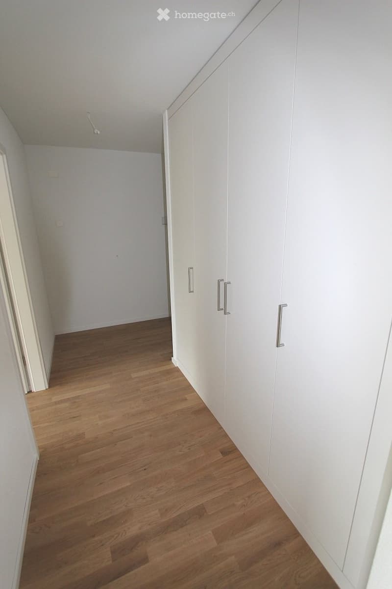 Empty room with light wooden flooring, white walls, and built-in white closet with silver handles.