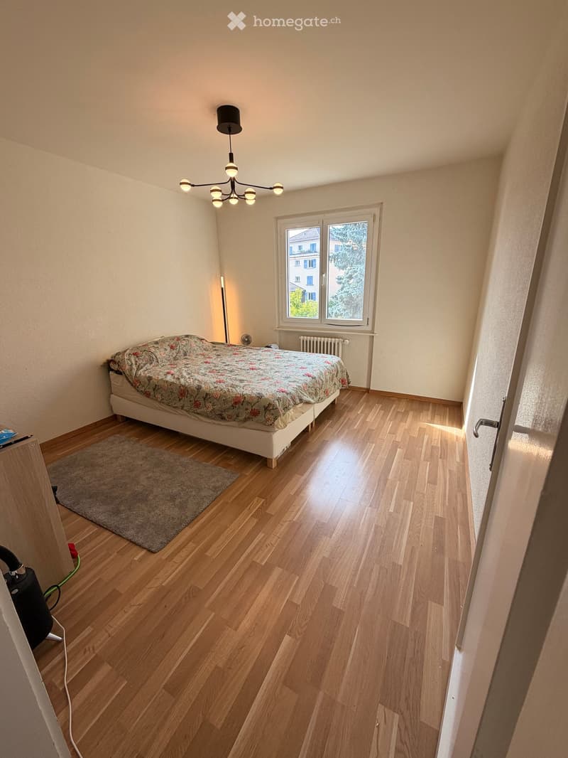 Bedroom with wooden flooring, a bed with floral bedding, a gray rug, a radiator, a fan, and a chandelier light fixture.