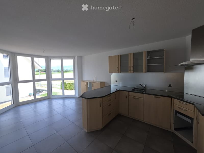 Modern kitchen with light wooden cabinets, black countertops, and stainless steel appliances. Large windows provide natural light and a view of the garden.