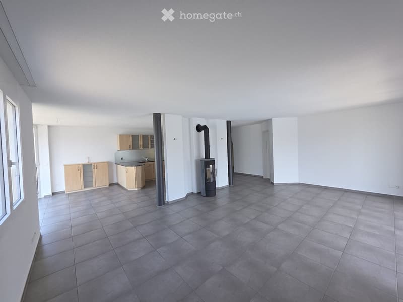 Open-plan space with tiled floor, light wooden cabinets, sink, and a wood stove in the center.