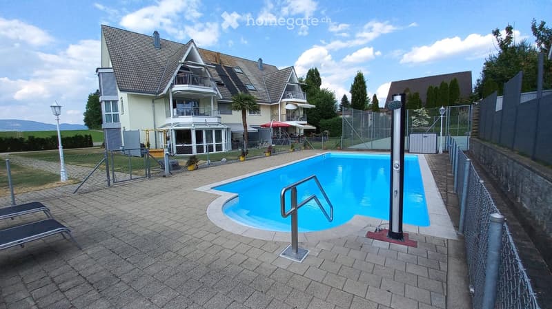 Outdoor area with a swimming pool, lounge chairs, and a modern house in the background.