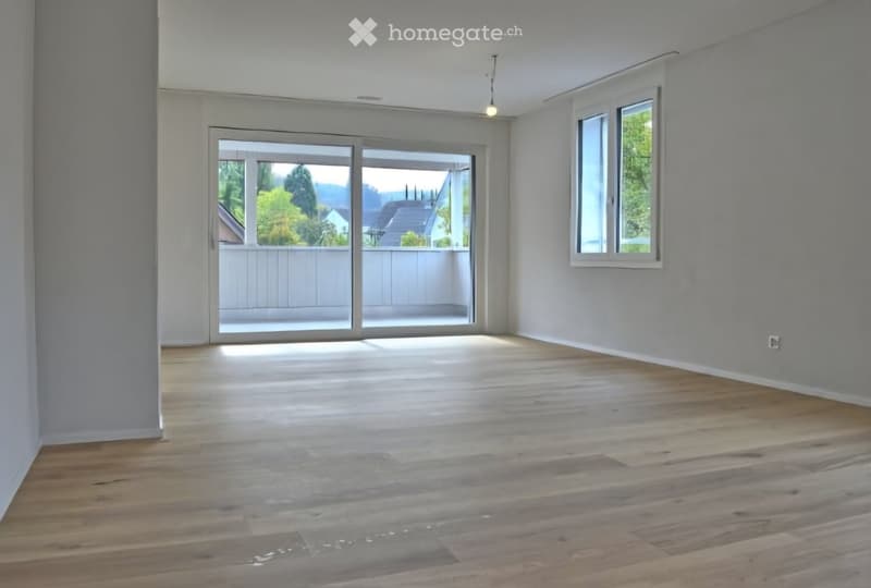 Empty room with wooden flooring, large sliding glass doors leading to a balcony, and a window on the right side.
