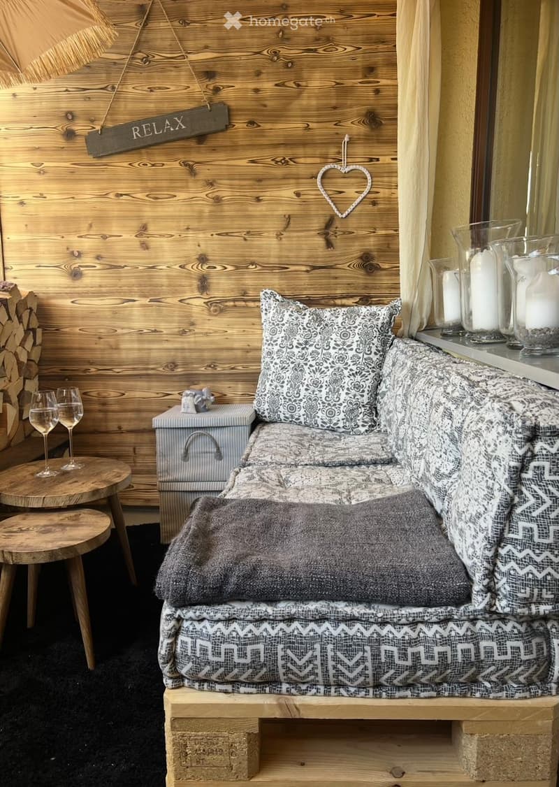 Cozy living room with a patterned sofa, wooden table, wine glasses, candles, and a wooden sign that reads "RELAX".