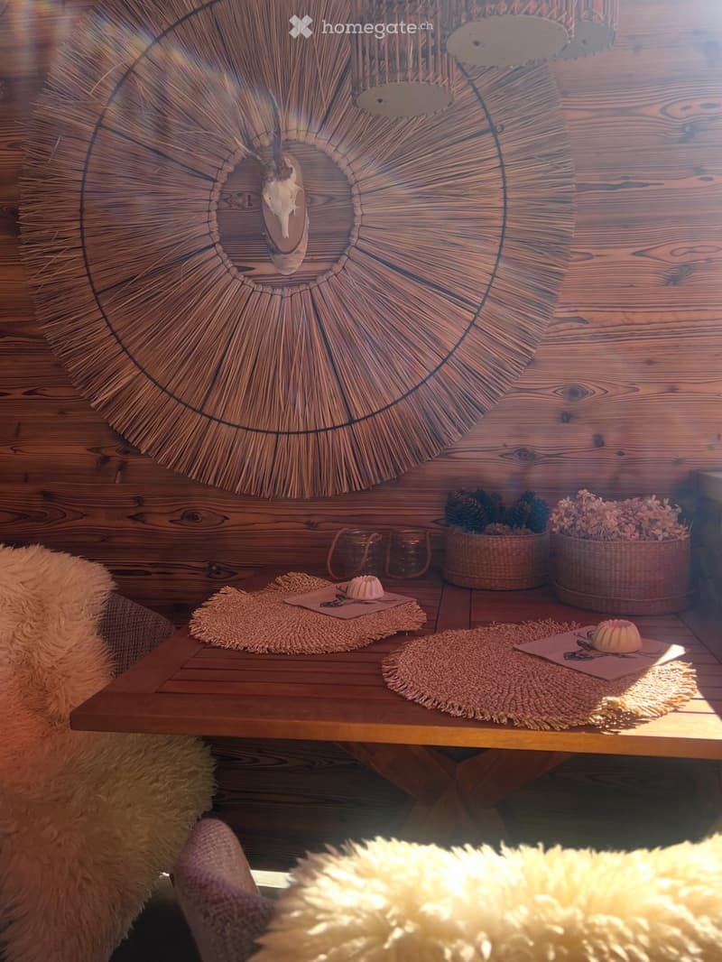 A cozy, rustic living space with a wooden table, woven rugs, baskets, and a decorative wall piece.