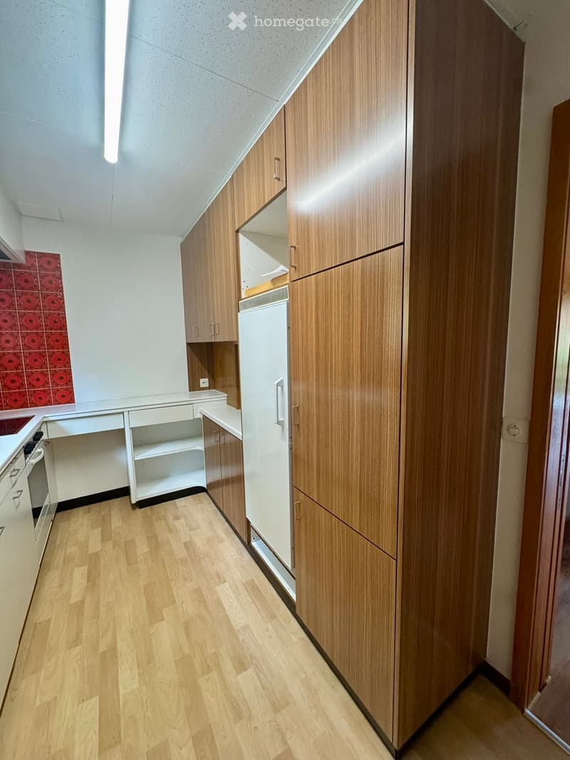 Modern kitchen with light wooden cabinets, white appliances, and a red-tiled backsplash. The space features a sleek, contemporary design with ample storage and a clean, organized layout.