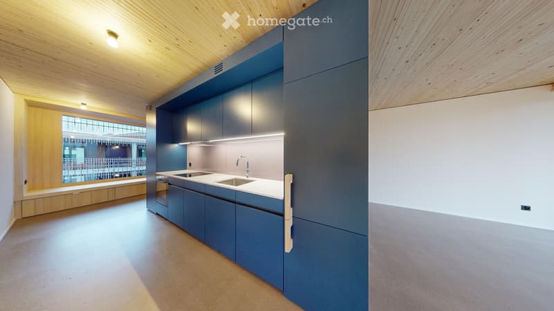 Modern kitchen with sleek blue cabinets, white countertops, and a double sink under a window. The space features a wooden ceiling and ample natural light.