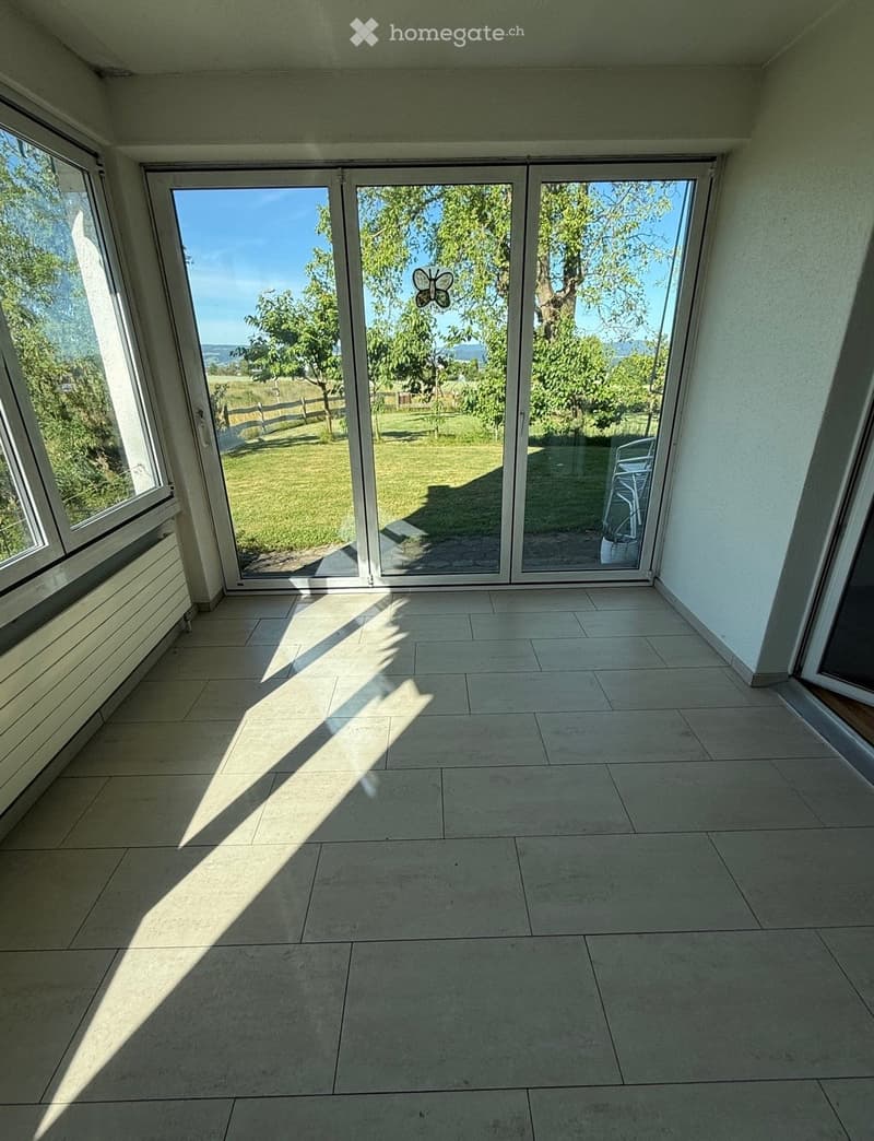 Empty room with large sliding glass doors leading to a grassy outdoor area, tiled floor, and natural light streaming in.