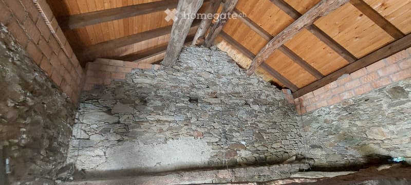 An attic space with exposed wooden beams and a stone fireplace base, no furniture or furnishings present.