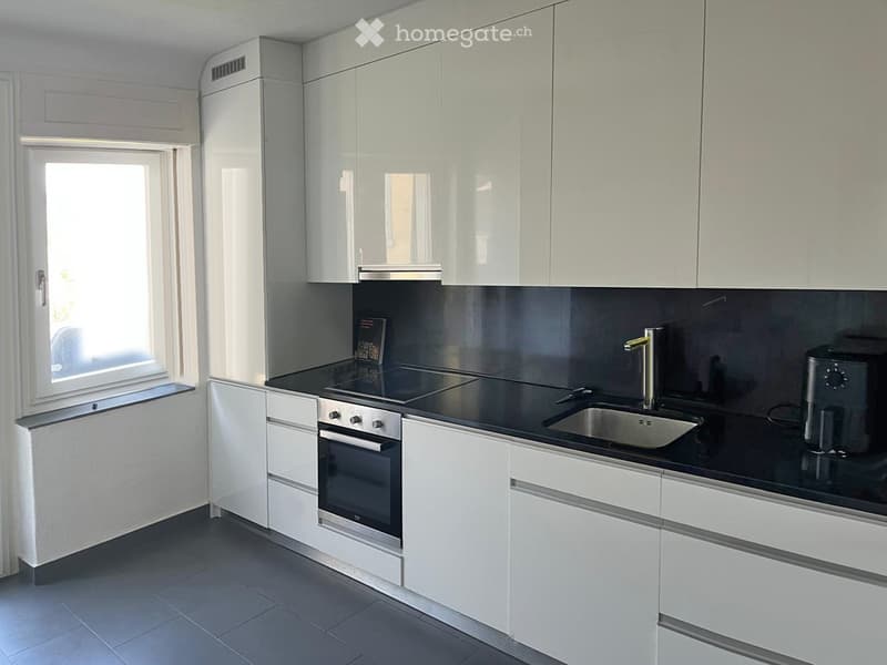 Modern kitchen with white cabinets, black countertops, stainless steel appliances, and a window providing natural light.