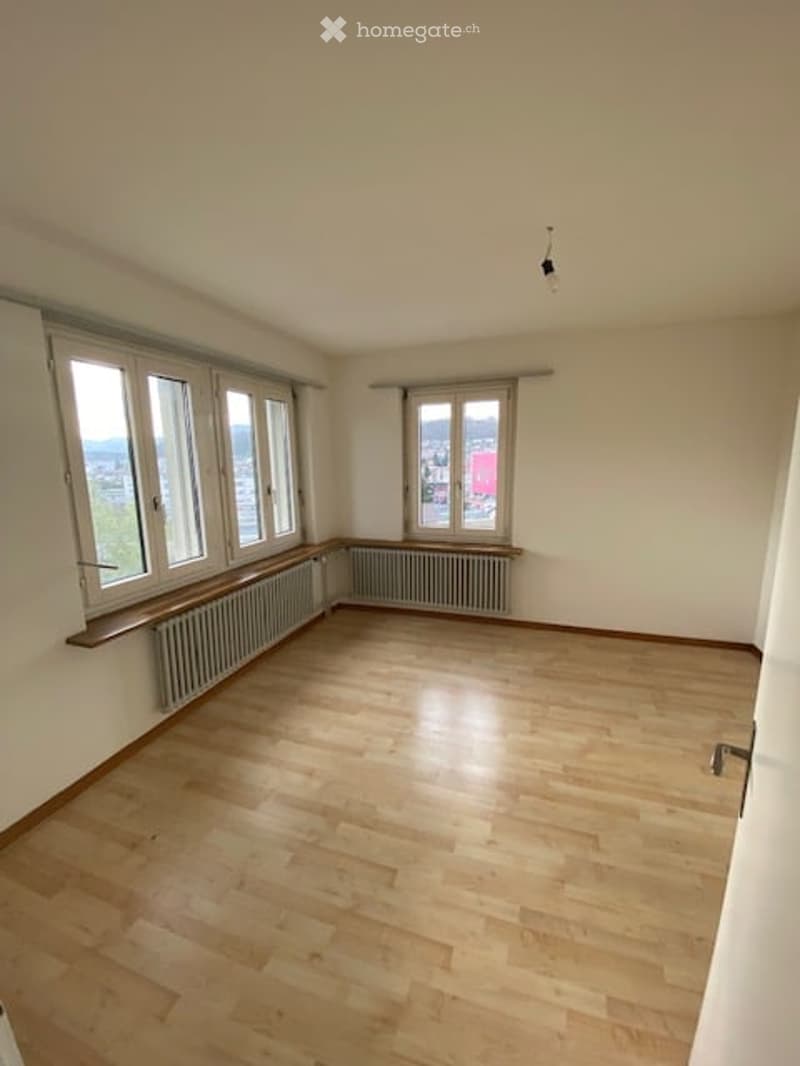 Empty room with wooden flooring, white walls, large windows, radiators, and a light fixture on the ceiling.