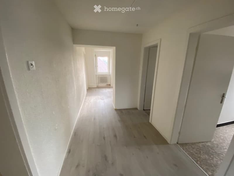 Empty hallway with wooden flooring, white walls, and open doors leading to other rooms.